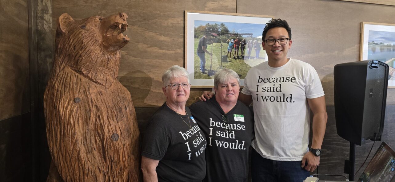 Three Camp Because I Said I Would volunteers standing beside a carved wooden bear.